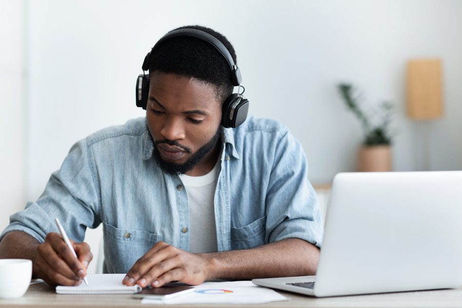 Mann mit Kopfhörern lernt am Laptop und macht sich Notizen
